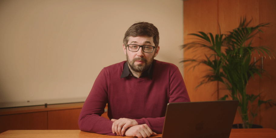 Image of Finbarr Curran in a red and black sweater, sitting at table with a laptop