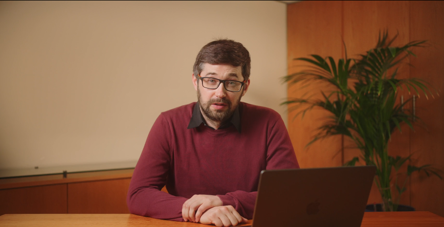 Image of Finbarr Curran in a red and black sweater, sitting at table with a laptop