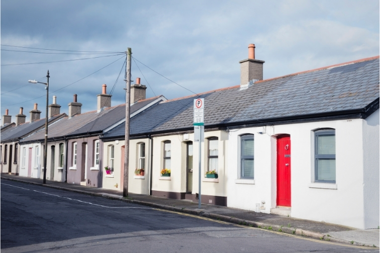 Row of cottages on a street with a white cottage with a red door in the foreground