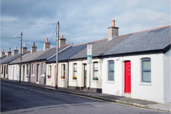 Row of cottages on a street with a white cottage with a red door in the foreground